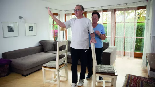 älterer Mann bei einer Bewegungsintervention in einer Wohnung mit einer älteren Dame